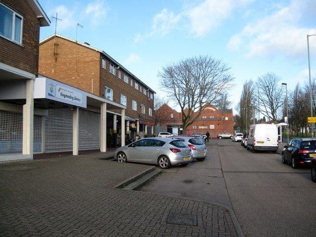 Kingstanding Library and the shopping parade under its flat canopy in January 2018, with parked cars along the kerb