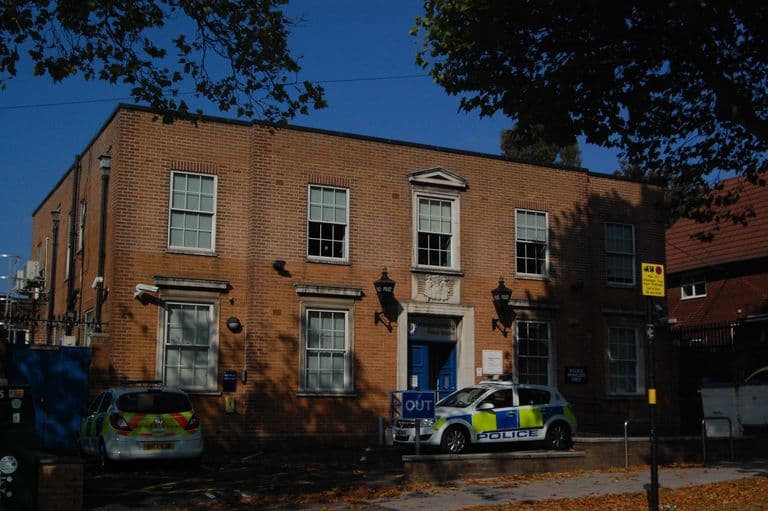 Neo-Georgian two-storey brick police station with a stone doorcase, carved panel over the door, blue lamps and police cars outside