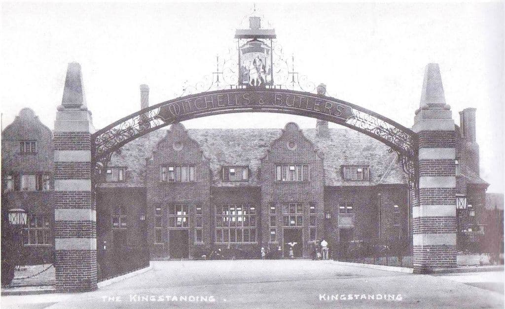 1936: The Kingstanding pub behind a tall iron arch lettered Mitchells & Butlers, with a hanging sign of a rider on a white horse, striped brick piers and Dutch gables