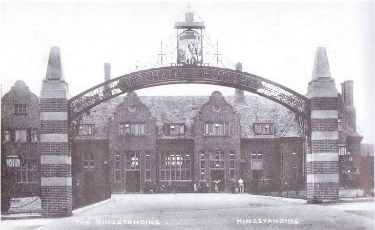 The Kingstanding pub behind a tall iron arch lettered Mitchells & Butlers, with a hanging sign of a rider on a white horse, striped brick piers and Dutch gables