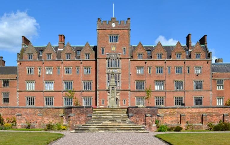 The red-brick front of St Mary’s College, Oscott, with its central clock tower above steps and a lawn