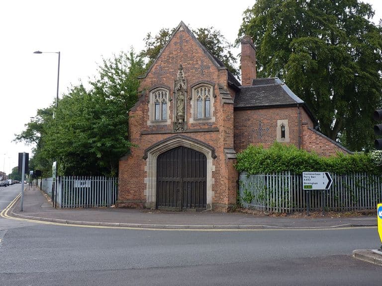 Gothic Revival brick gatehouse with a carved stone arch, niche statue and tall chimney at the junction of Chester Road and College Road