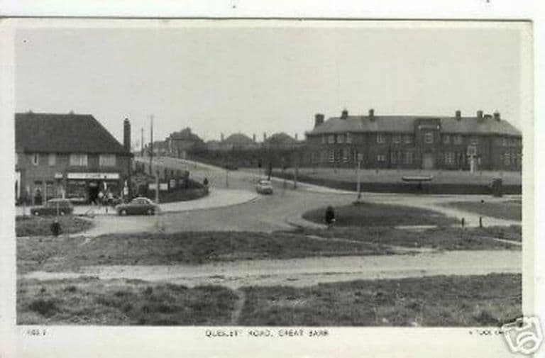 A postcard view of Queslett Road: a corner shop at left, a roundabout and grass verges, and a long block of houses on the rise behind