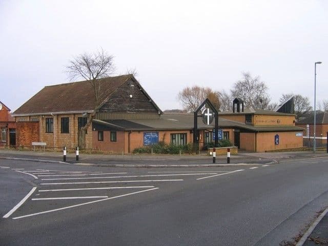 Low modern brick and timber church centre with a cross sign on a corner, overlooking a large road junction