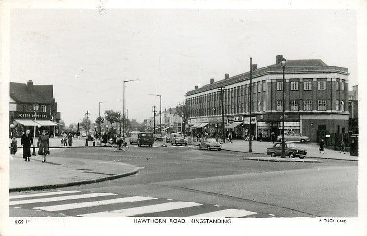 1950: Black-and-white postcard of Hawthorn Road, Kingstanding, around 1950: shoppers and cyclists by a large shopping block, parked cars, and Foster Brothers on the corner