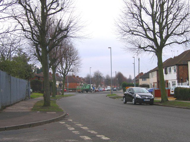 A wide suburban road with bare trees and houses, looking towards a junction