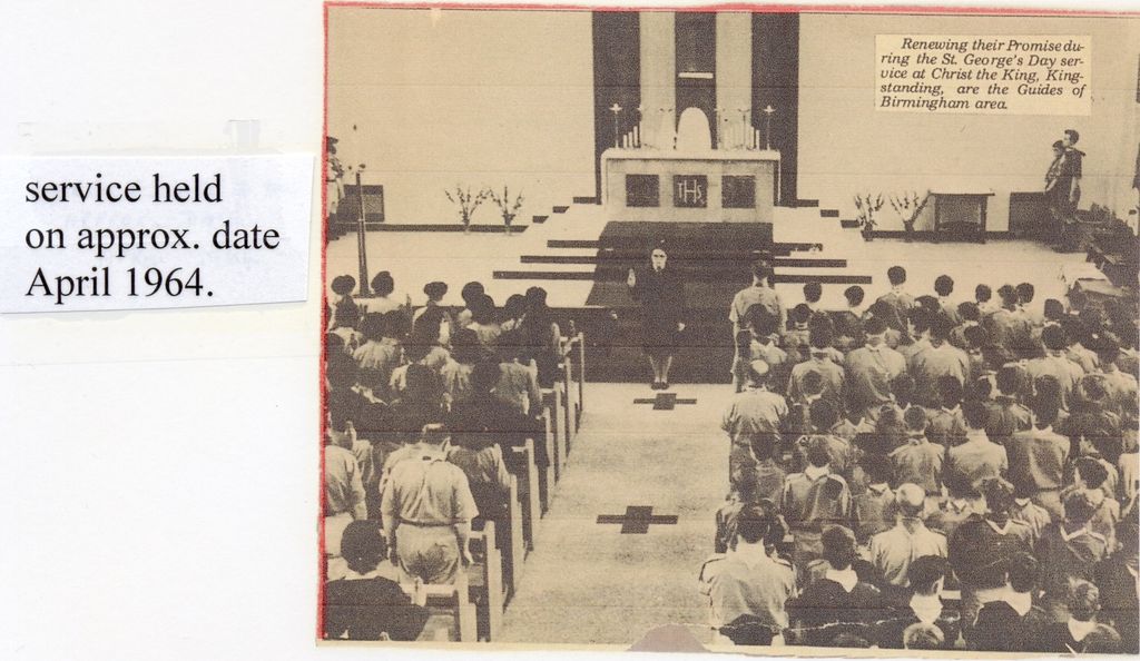 A newspaper photograph of a church interior: rows of uniformed Guides in the pews and aisle face the altar steps, where a leader stands with her hand raised. The printed caption reads “Renewing their Promise during the St. George’s Day service at Christ the King, Kingstanding, are the Guides of Birmingham area.” A typed label beside it says “service held on approx. date April 1964.”