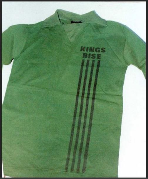 Colour photograph of a green long-sleeved collared sports shirt with “KINGS RISE” and four vertical black stripes printed on the front.
