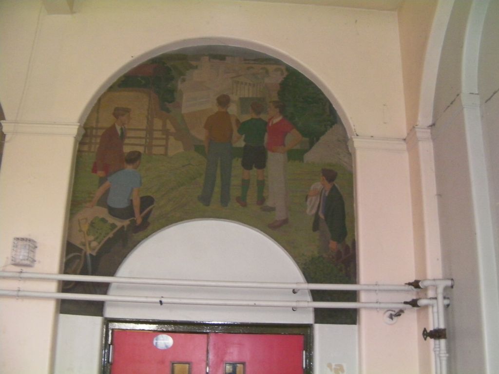An arched mural painted above a doorway: young men and boys in 1930s clothes stand in a field by haystacks and a wheelbarrow of vegetables, looking towards a city of classical buildings in the distance.