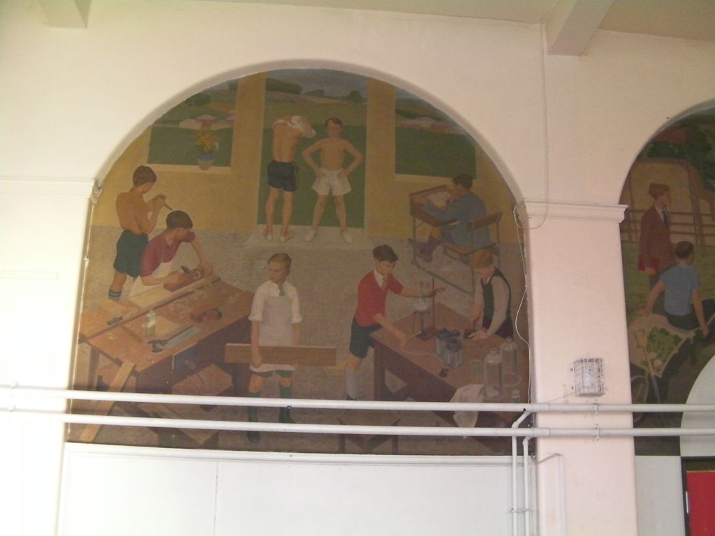 An arched mural of boys at school: planing wood at a carpentry bench, carrying a plank, doing a chemistry experiment and drawing at a desk, with two boys in shorts and gym shoes framed in a window above.