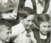 A very small crop from an old school group photograph showing a boy with short hair in a white shirt and tie.