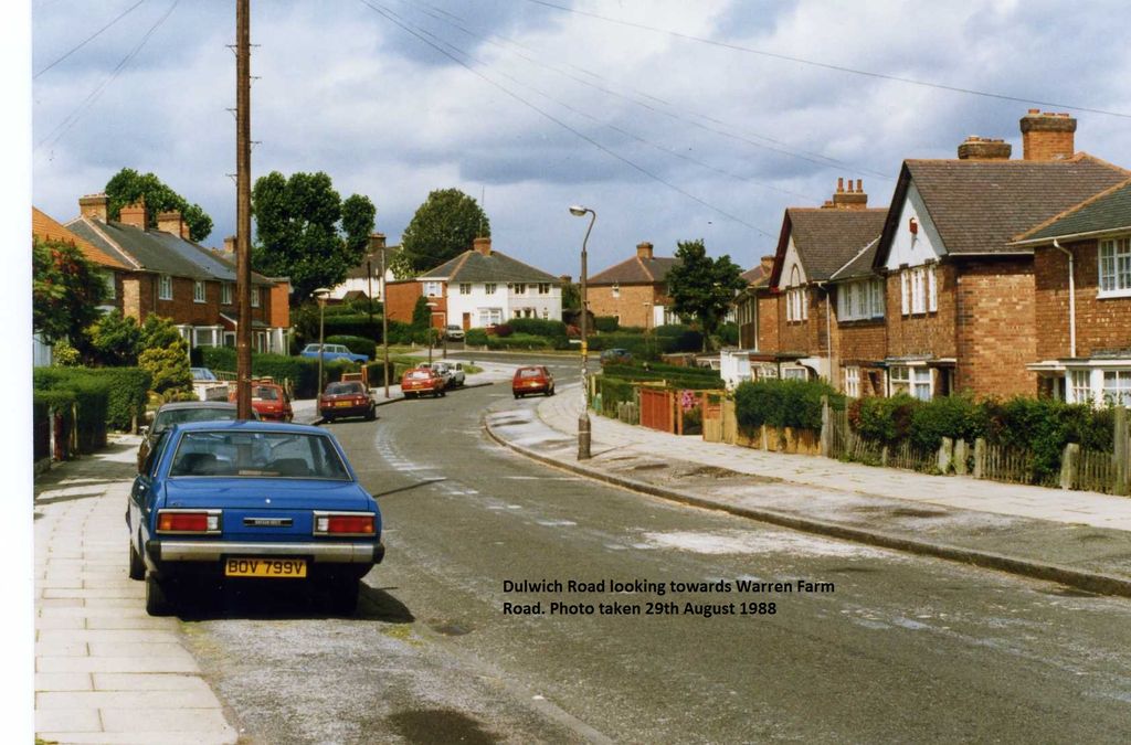Colour photo of Dulwich Road curving away between brick semi-detached houses with front hedges and fences, a blue Datsun saloon parked in the foreground and other cars further along; a caption is printed on the image.