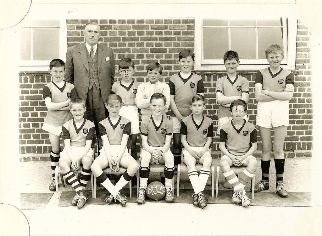 School football team of eleven boys in dark shirts with light collars and striped socks, with an older man in a three-piece suit; the ball is marked “1960-61”.