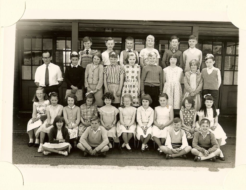 Class of about forty junior-school children in five rows, a young male teacher in a white shirt and tie standing at the left.