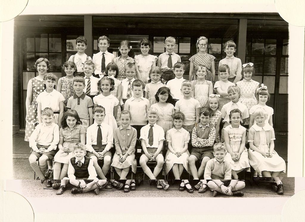 Class of about forty-five junior-school children in five rows, a young woman teacher standing at the left, two boys sitting cross-legged in front.