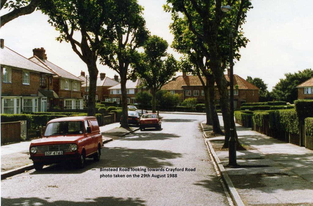 Colour photo of a tree-lined Binstead Road curving between brick semi-detached houses with hedges, a red Mini van parked on the left; a caption is printed on the image.