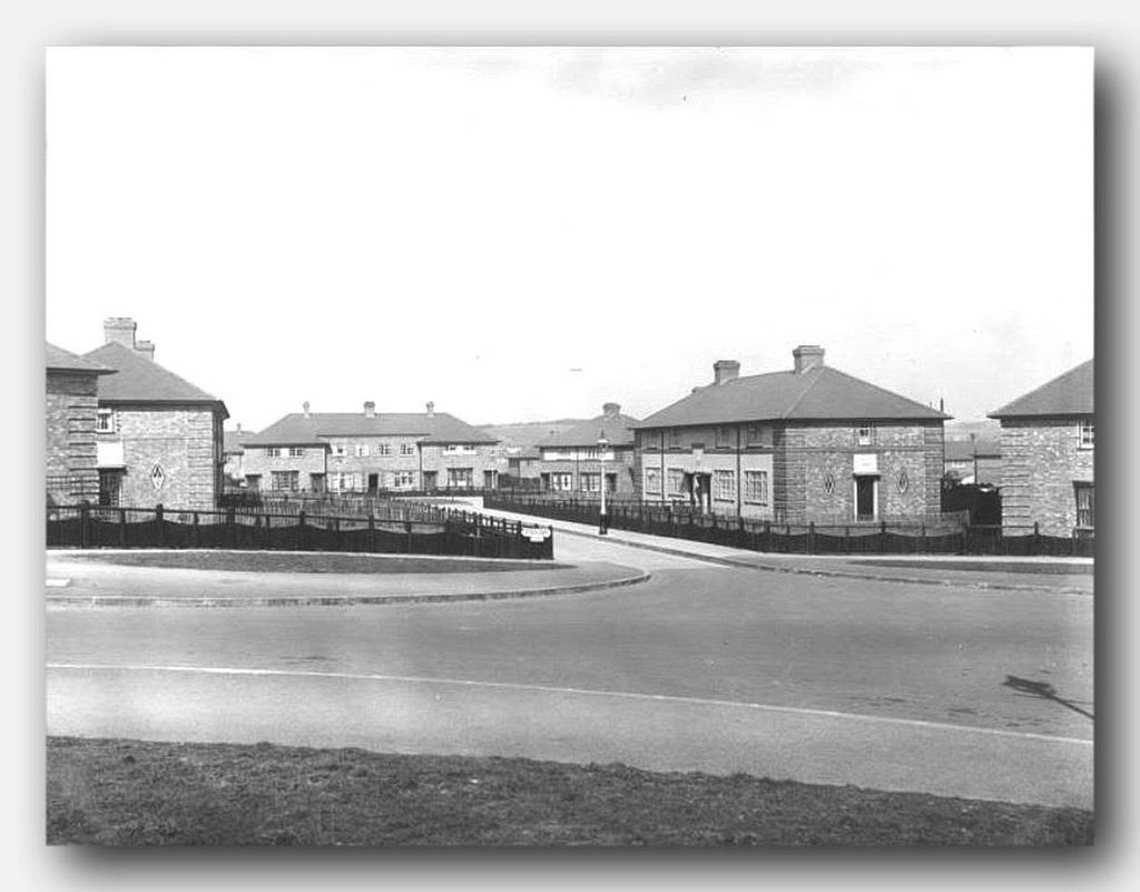 A road junction on the new estate: brick houses with diamond motifs, wooden fences and a road rising into the distance