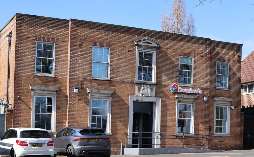 The same neo-Georgian brick former police station with a Domino's sign on the front and cars parked outside, March 2025