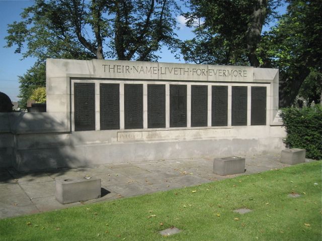 Pale stone screen wall with nine dark name panels under the words 'Their name liveth for evermore', on a paved terrace in Witton Cemetery, with trees behind.