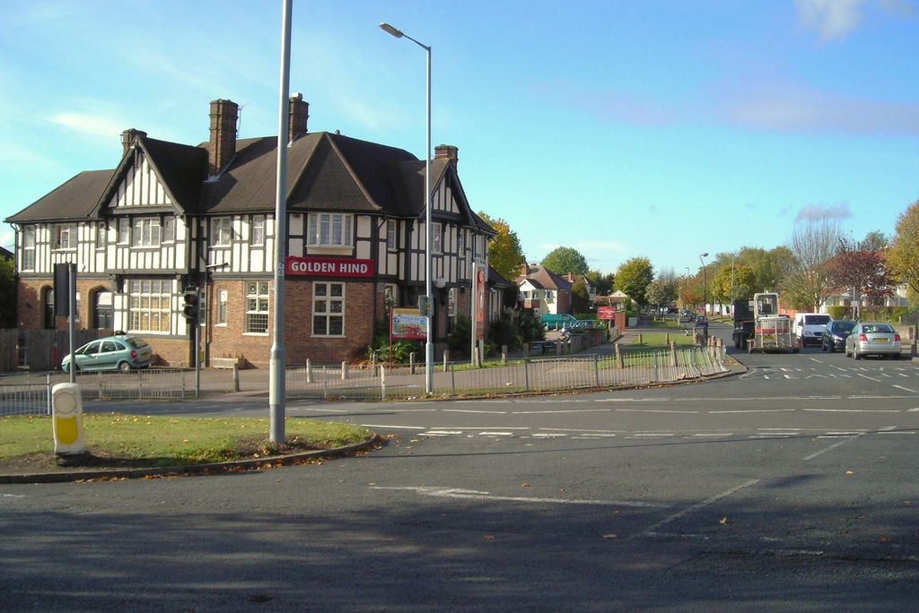 Mock-Tudor black-and-white gabled pub, the Golden Hind, on a street corner with traffic lights and a tree-lined road beyond