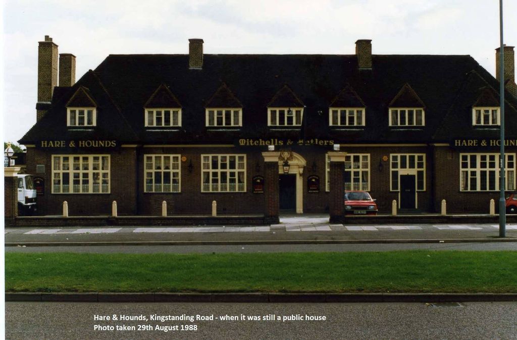 The long front of the Hare & Hounds pub with seven dormer windows, the names Hare & Hounds and Mitchells & Butlers in gold, and a grass verge in front