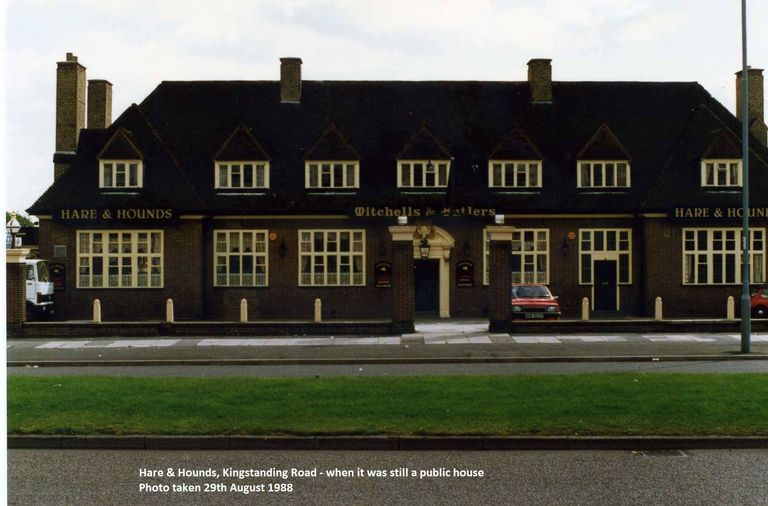 The long front of the Hare & Hounds pub with seven dormer windows, the names Hare & Hounds and Mitchells & Butlers in gold, and a grass verge in front