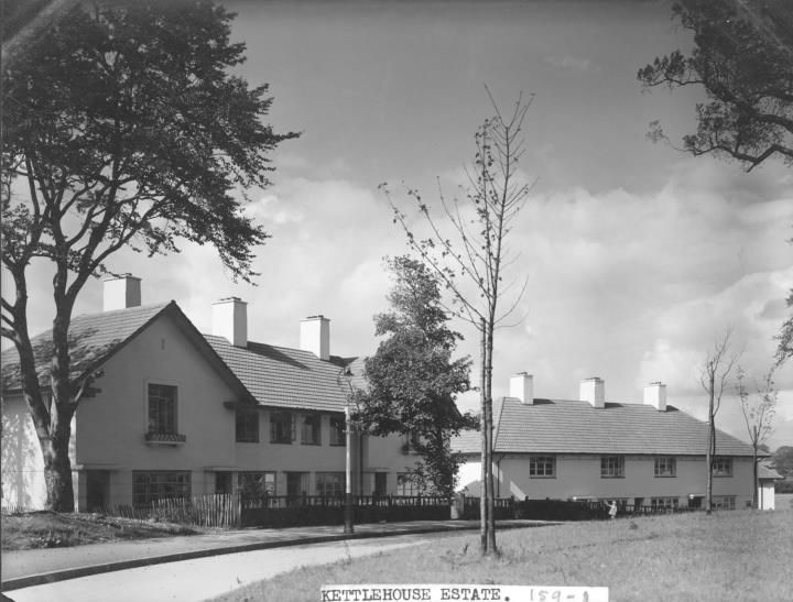 Houses with steep gables and tall chimneys beside a path and young street trees; the print is captioned Kettlehouse Estate.