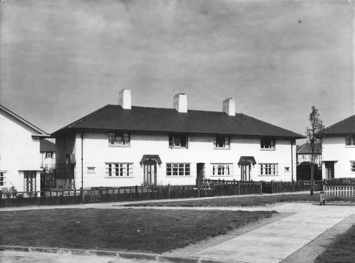 A terrace of white rendered houses facing a lawn with a bench, flanked by further houses.