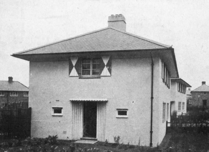 A square rendered house with a hipped roof, diamond-patterned shutters and a fluted surround to the front door.