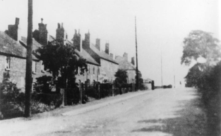 A row of old cottages with tall chimneys along a lane, with a telegraph pole in the foreground.