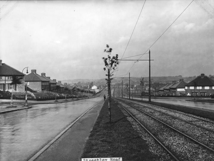 A wide road with a central tram reservation, overhead wires and young trees, lined with new houses; the print is captioned Streetley Road.