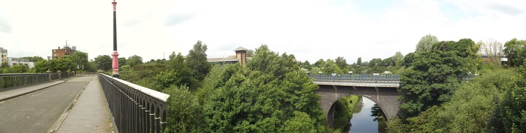 Panoramic view of a single-span cast-iron bridge over a deep canal cutting.