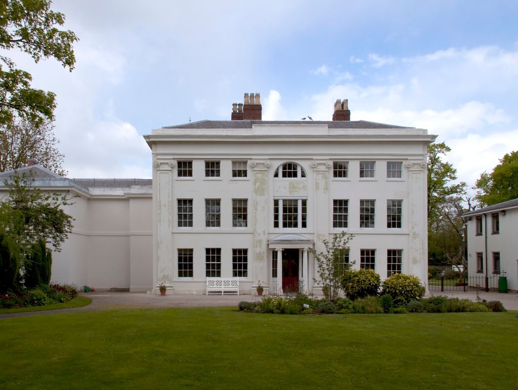 The white-painted front of Soho House, with rows of tall windows and a central doorway, behind a lawn.