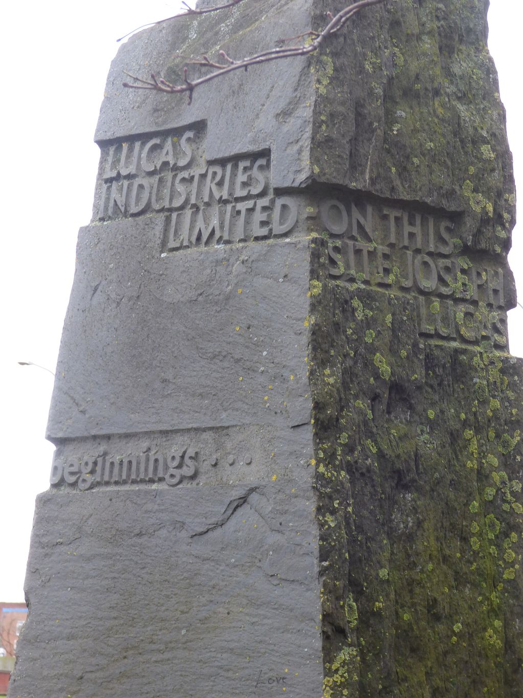 A tall, weathered slate block carved with the words Lucas Industries Limited, On this site Joseph Lucas, and From small beginnings.