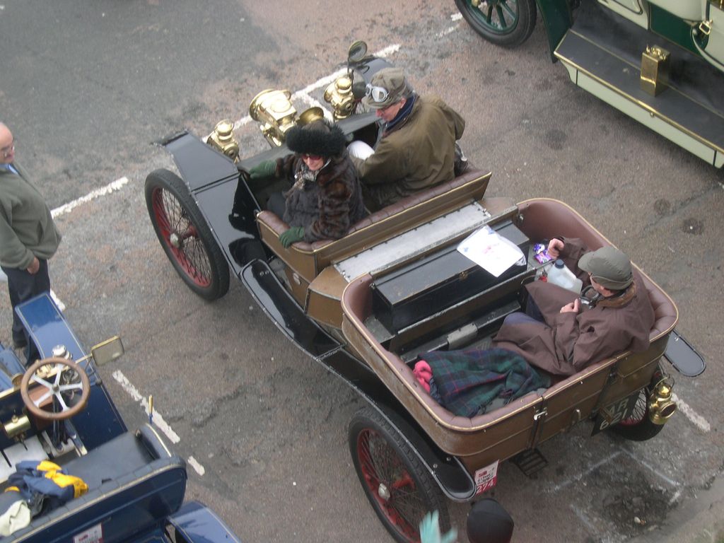 An open veteran car with brass lamps and a rear passenger compartment, seen from above, with its crew aboard.