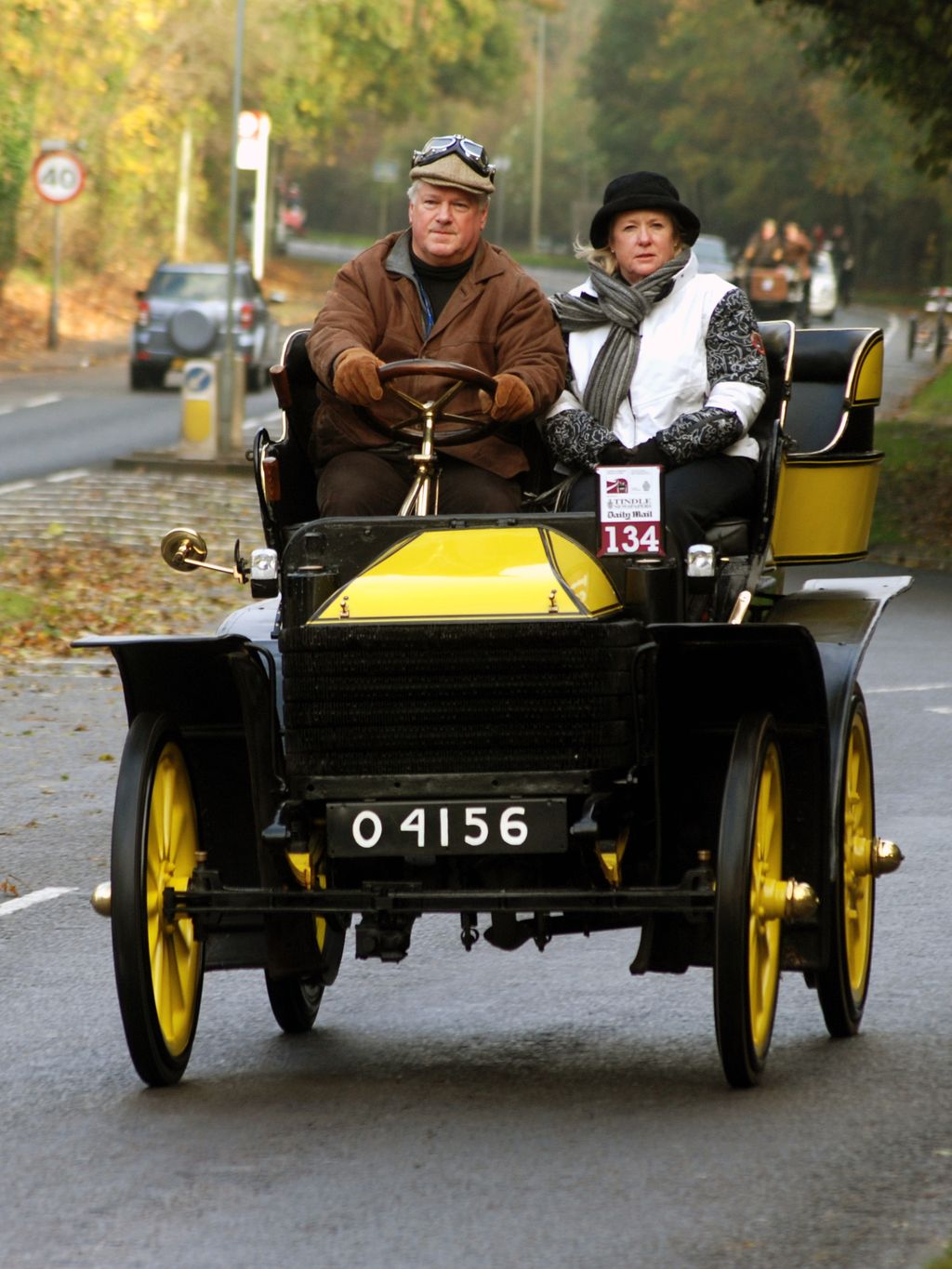 A black and yellow veteran car carrying a man and a woman along a road during the London to Brighton run.