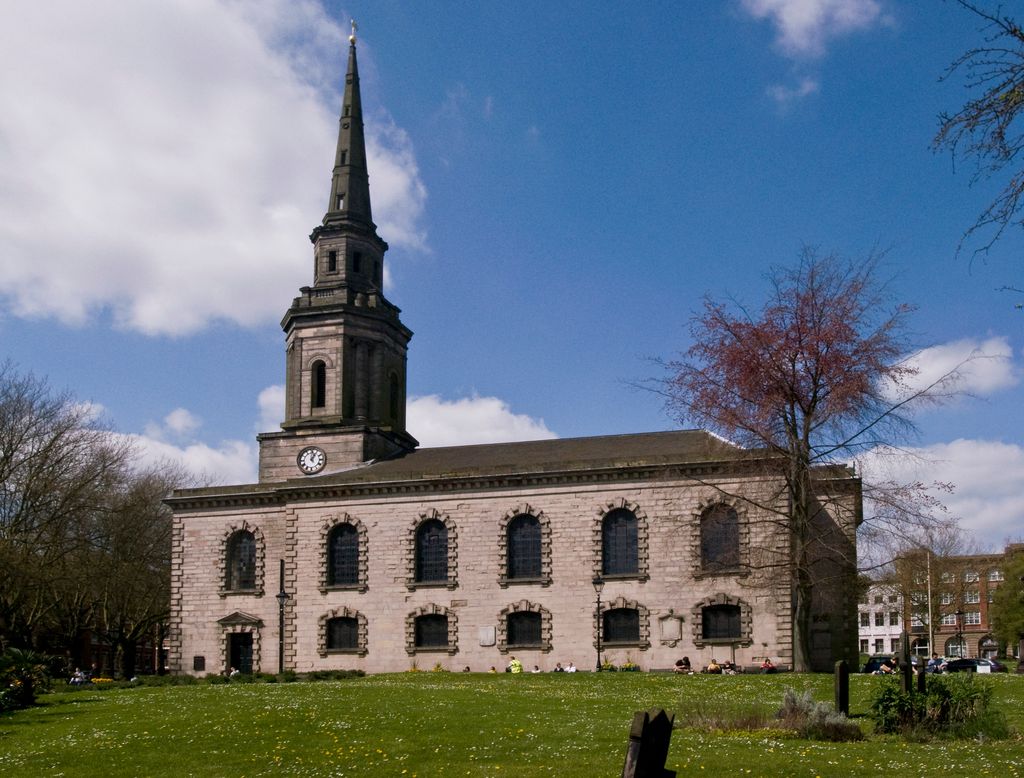 A Georgian stone church with tall round-arched windows and a slender spire, seen across its churchyard.