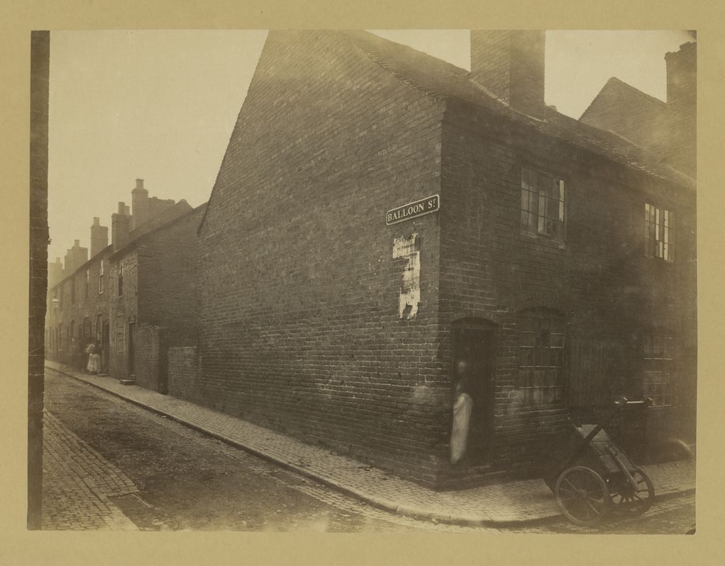 Old photograph of a narrow street of shabby brick houses.