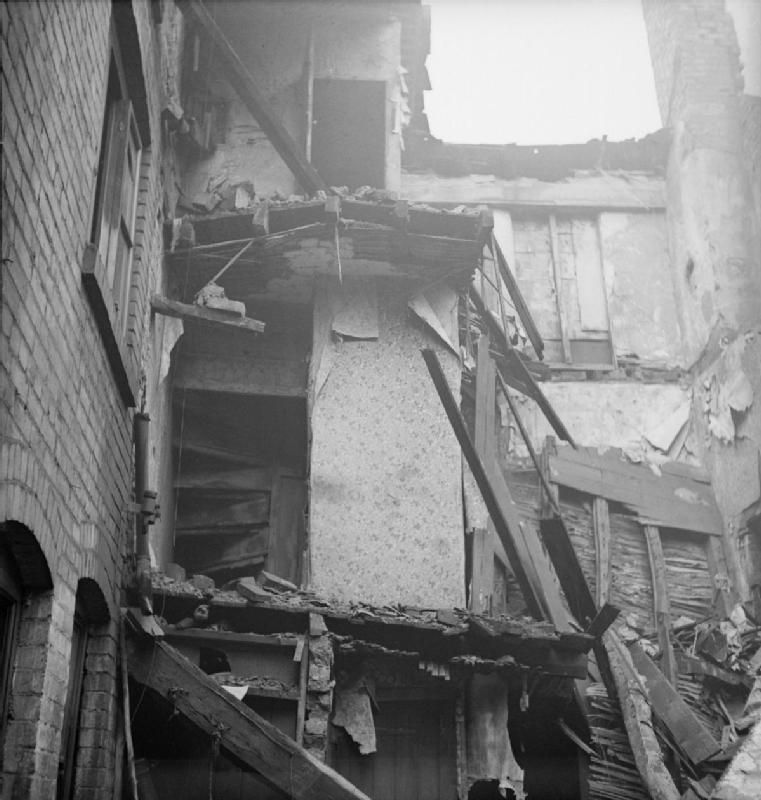 Wartime photograph of a terraced house with its side wall blown away, showing the staircase and wallpaper.