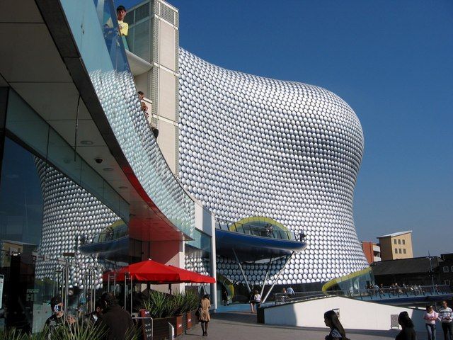 Curved building covered in shiny metal discs on a blue background.