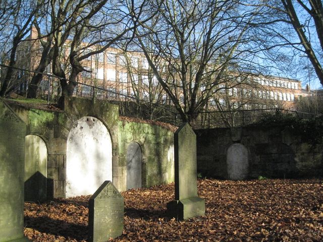 A curving wall of blocked catacomb entrances set into a hillside in a cemetery.