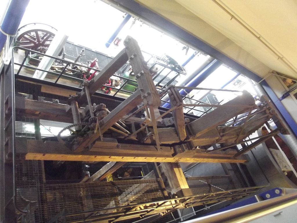 A large eighteenth-century beam engine with a wooden beam and iron cylinder in a museum gallery.