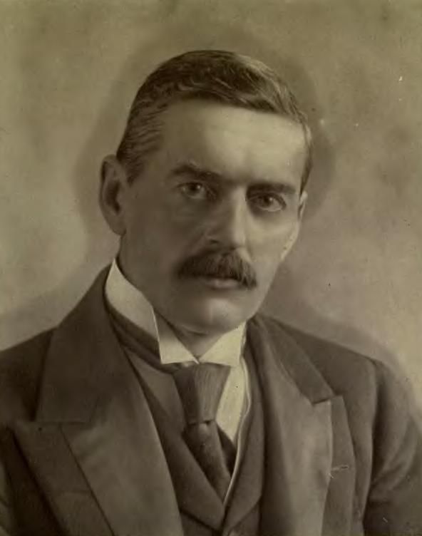 Sepia photograph of a man with dark hair and a moustache, in a three-piece suit and stiff collar.