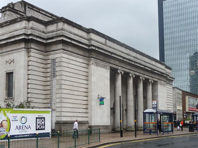 The colonnaded stone side and front of the former Municipal Bank on a street corner, behind railings and hoardings.