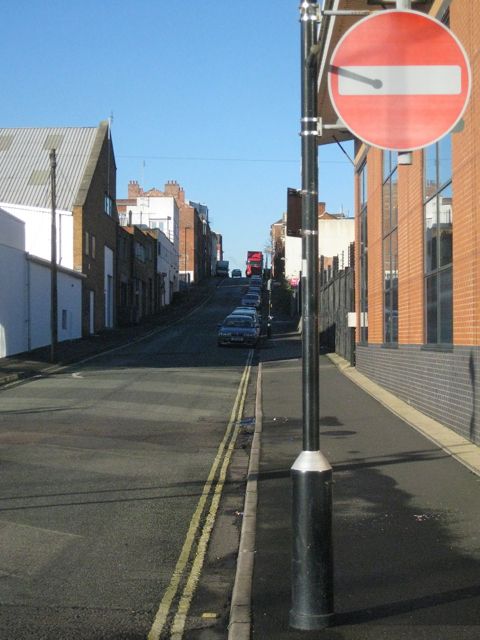 A narrow street sloping between old brick buildings and a modern block, with a no-entry sign.