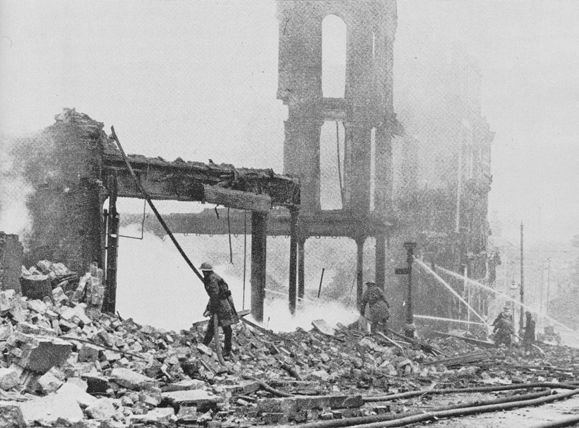 Firemen hosing smouldering ruins.