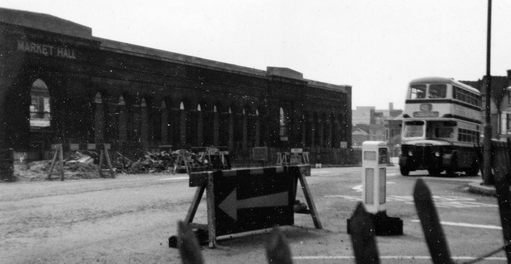 Photograph of the stone side wall of the bombed Market Hall beside a newly widened road.