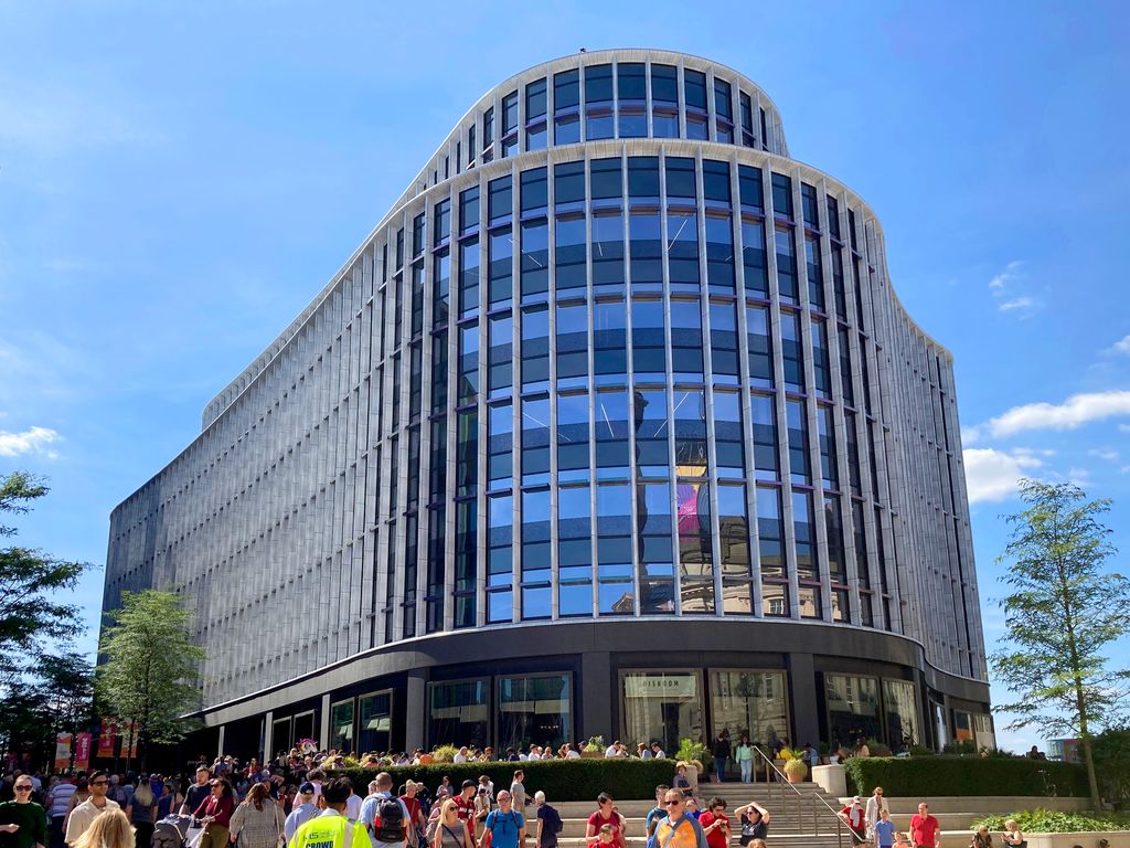 A modern stone-and-glass office building beside a paved square.