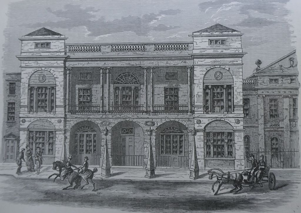 Engraving of a classical theatre front with arched doorways, paired columns and a balustrade, horses and a carriage in the street.