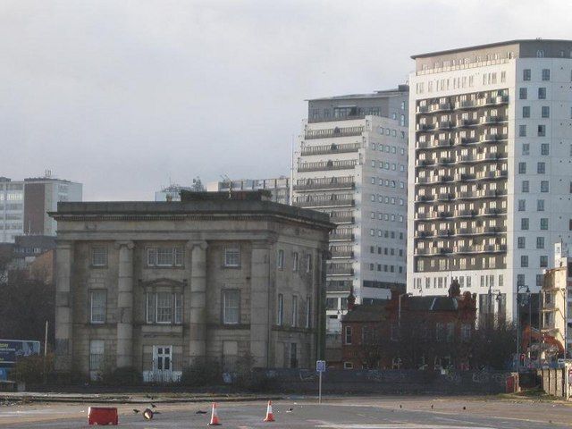A classical stone railway building on the left and a modern apartment block on the right.